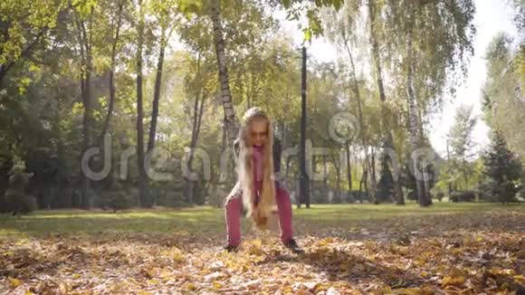 年轻开朗的白种人女孩在秋天的公园或森林里辗转着黄色的叶子可爱的少女视频的预览图