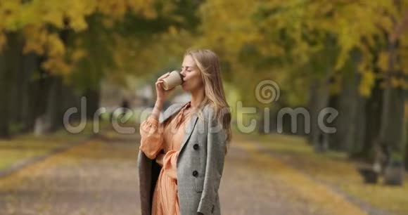优雅的高加索女人棕色长发穿着格子夹克在秋天的公园里喝咖啡美丽美丽视频的预览图