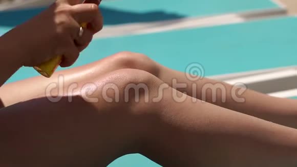 在炎热的夏天年轻女子正在游泳池旁的腿上涂防晒霜视频的预览图