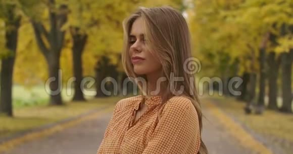 一个自信的高加索女人站在秋天公园的路上的肖像穿着芥末衣服的迷人女孩视频的预览图