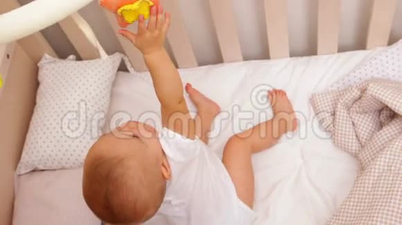 可爱的女婴站在童床上玩手机视频的预览图