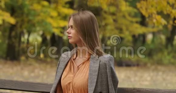 一位优雅的高加索女人坐在公园的长凳上微笑的肖像穿着格子衣服的迷人女孩视频的预览图