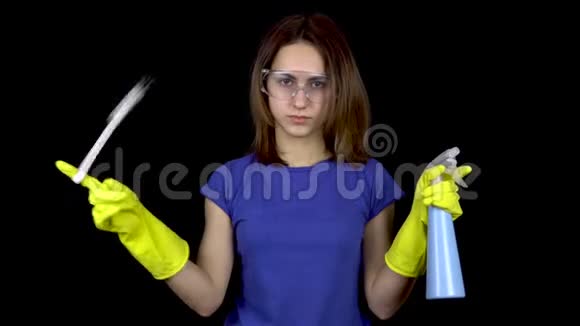 一个年轻的女人把马桶刷拧在她的手指上从一个喷雾瓶里喷水戴安全眼镜的女人视频的预览图
