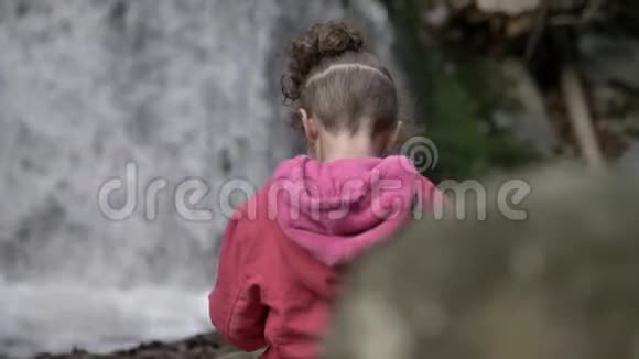 可爱可爱的小女孩有着有趣的发型在野外观看美丽的瀑布视频的预览图