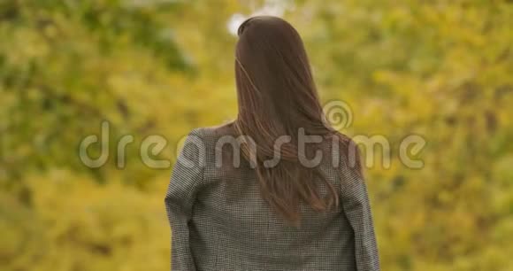 一位穿着格子夹克的白人年轻女子站在秋天公园的后景可爱的女孩转向视频的预览图