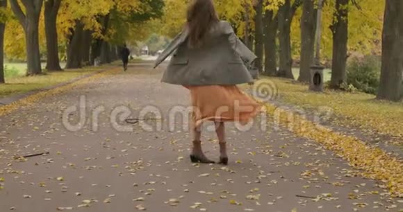 迷人的高加索女孩棕色长发和灰色的眼睛在秋天的公园里旋转穿着芥末衣服的优雅女孩视频的预览图