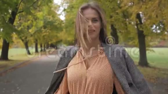 一位身材苗条的高加索女人穿着格子夹克和芥末裙转身在路上漫步视频的预览图