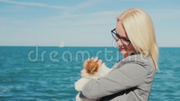 一个女人在大海的背景下抱着一只小狗远处可以看到游艇视频的预览图