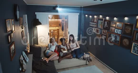 高角度美丽幸福多民族女性朋友在家看电视大屏幕上用投影仪慢动作视频的预览图