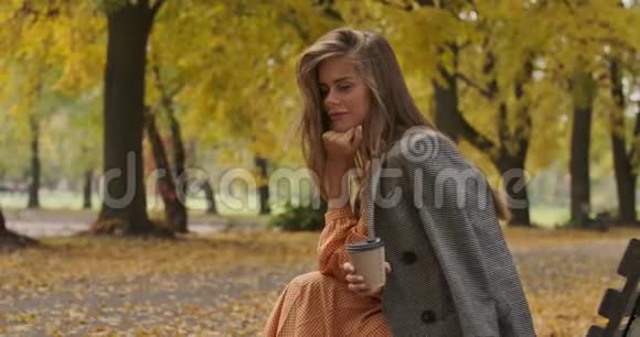 秋天公园里坐在长凳上的棕色长发和绿色眼睛的迷人白种人女性的侧面景色视频的预览图