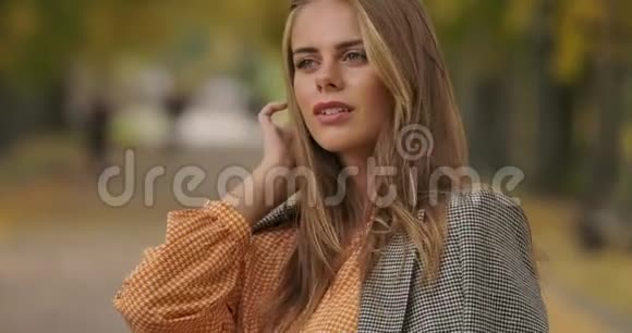 一幅美丽的高加索女人站在秋天公园里挽着头发的特写肖像穿格子夹克的漂亮女孩视频的预览图