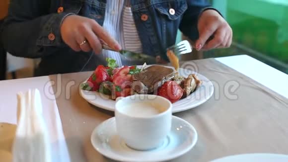 一个女孩在咖啡馆里吃早餐她用刀子切蔬菜视频的预览图