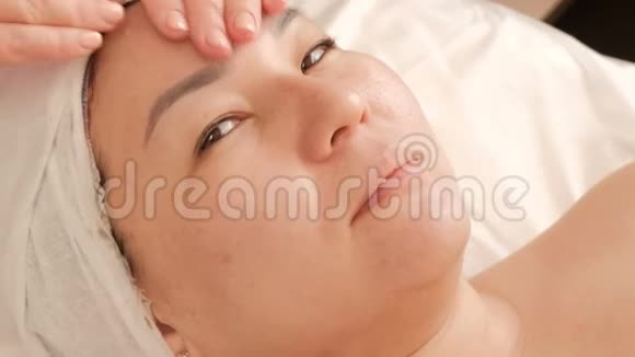 亚洲美容院的面部按摩美容师的双手将面霜涂在东方中脸上视频的预览图