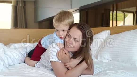 一个女人和她的儿子在家里躺在床上的肖像孩子坐在后面视频的预览图