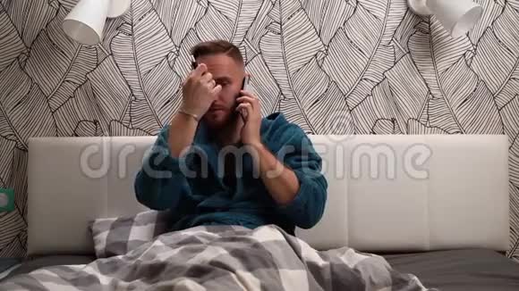 穿着绿色或深蓝色浴袍的大胡子男人在电话旁交谈在床上抽烟视频的预览图