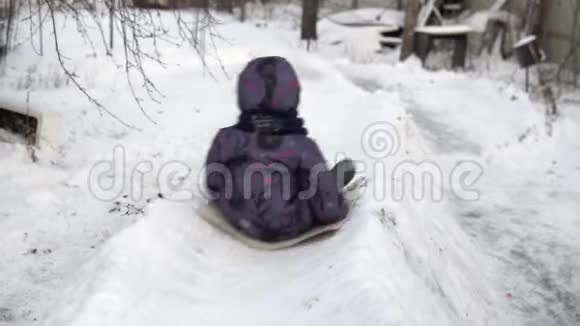 一个孩子在雪地滑梯上翻滚冬天在街上玩在寒冷的冬天孩子穿着一件夹克和一件视频的预览图