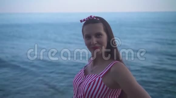一个穿着红色衣服的女孩在海和天空的背景下给一个相机送一个吻视频的预览图