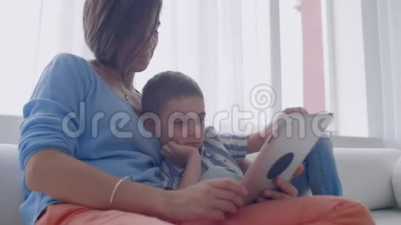 母子俩在家玩数字平板电脑年轻的母亲带着她5岁的孩子带着数码平板电脑微笑视频的预览图