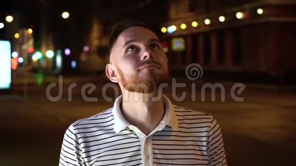 有胡子的帅哥抬起头然后在镜头里穿着条纹马球衫晚上站在街上视频的预览图