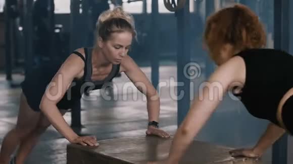 快乐迷人的年轻金发女人在健身房和女健身教练一起做俯卧撑慢动作视频的预览图