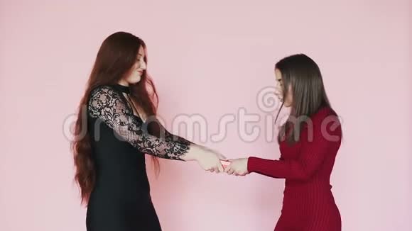 两个年轻女孩为了礼物而打架拉对方礼盒慢动作的粉红色背景视频的预览图