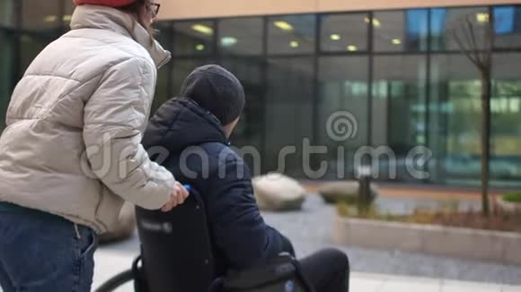 年轻的女人带着一个年轻人坐轮椅中风后恢复康复中心背面视频的预览图