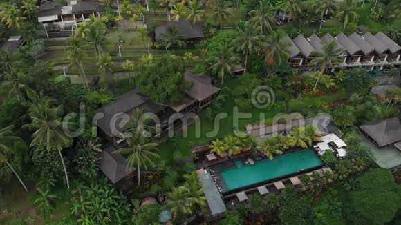 从空中俯瞰豪华酒店带草屋顶别墅和热带丛林的游泳池棕榈树稻田视频的预览图