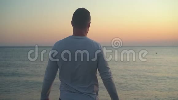 一个年轻人站在海上日落的背景上举起双手显示出自由的迹象视频的预览图