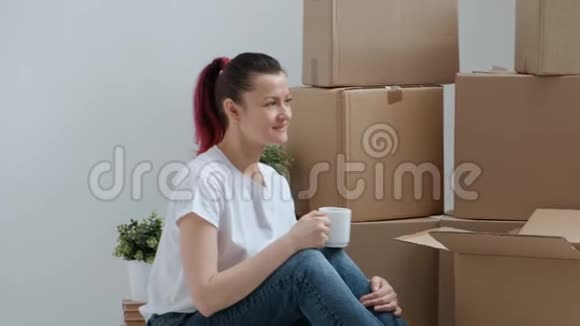 穿着牛仔裤和白色T恤的年轻美女正在地板上喝咖啡背景是视频的预览图