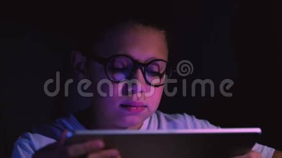 可爱的小男孩在黑暗的房间里用平板电脑视频的预览图
