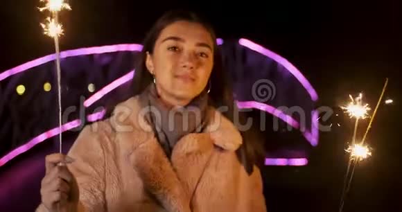 快乐女孩模特看起来手里拿着火花微笑的年轻女子庆祝新年的霓虹灯背景视频的预览图