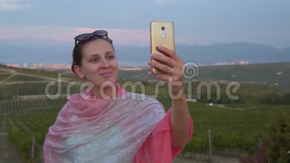 一个年轻的女孩走在山上附近的葡萄园中在电话里自拍视频的预览图