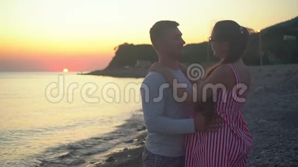 一对年轻的夫妇站在海上日落的背景上一男一女站着微笑着亲吻着视频的预览图