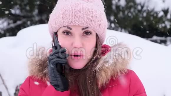 在一个阳光明媚的冬天微笑的年轻女子在一个冬天的公园里打电话穿红色夹克的女人视频的预览图