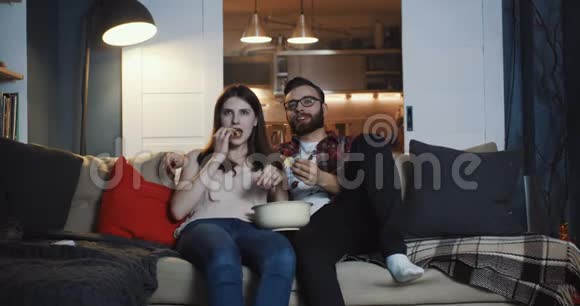 快乐的年轻休闲欧洲浪漫情侣在家看电视剧微笑着说话吃爆米花慢动作视频的预览图