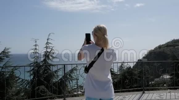 一个女人走在海边美丽的公园里用智能手机制作视频视频的预览图