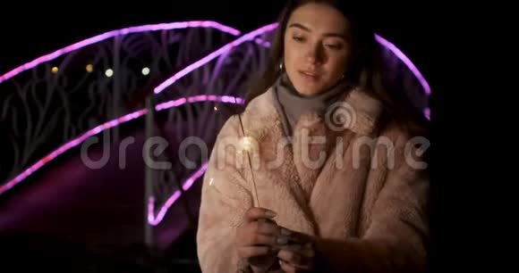 快乐女孩模特看起来手里拿着火花微笑的年轻女子庆祝新年的霓虹灯背景视频的预览图