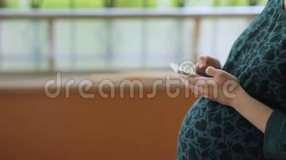 年轻漂亮的孕妇穿着绿色复古的t恤在智能手机上发短信视频的预览图