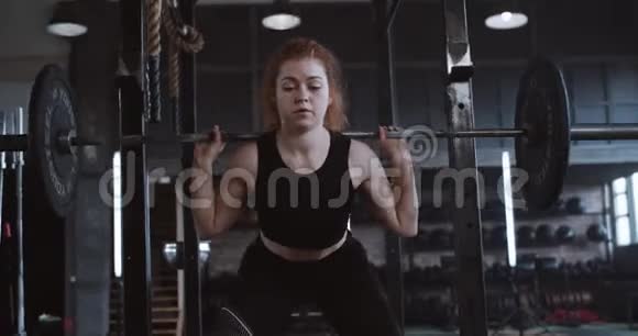 年轻漂亮的白种人红头发运动女子举起沉重的杠铃站在大型专业健身房慢动作视频的预览图