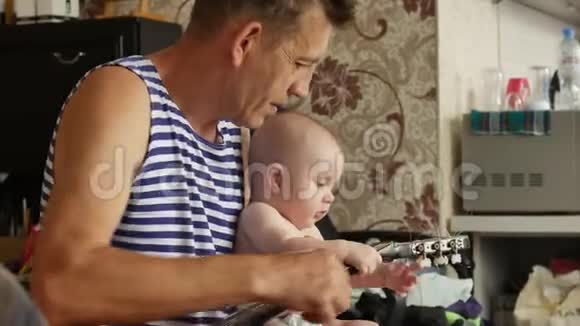爷爷正在向他的小孙子展示如何在家里弹吉他而这个孩子好奇地摸着琴弦他们视频的预览图
