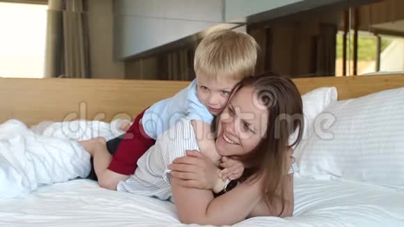 妈妈和儿子早上躺在床上男孩亲吻并拥抱他的母亲视频的预览图