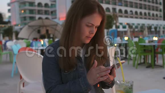 一位年轻女子的特写镜头手里拿着一部手机在一家街头咖啡馆休息视频的预览图