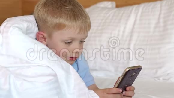 一个小男孩躺在毯子下手里拿着一个电话的特写镜头视频的预览图