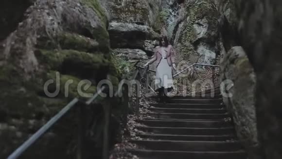 穿着春装的年轻美女跑下楼梯在岩石间大笑慢动作视频的预览图