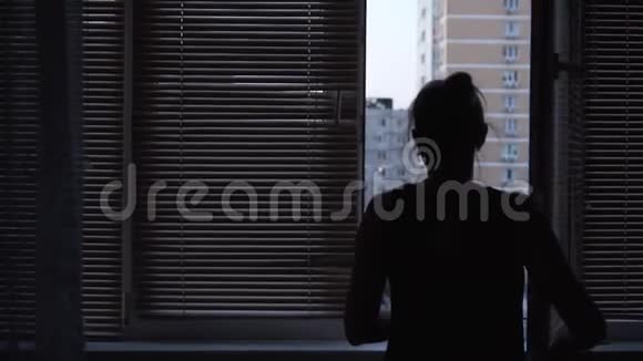 年轻的成年女人靠在窗户上用百叶窗关上窗户女孩关上窗户房间变暗了视频的预览图