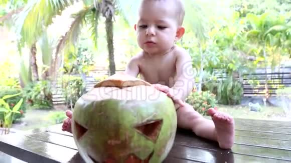 一个非常严肃的一岁婴儿从桌子上扔出新鲜的绿色椰子一张脸像万圣节南瓜一样刻在椰子上视频的预览图
