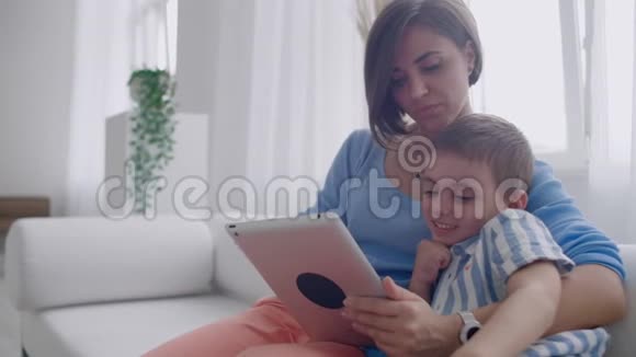 母子俩在家玩数字平板电脑年轻的母亲带着她5岁的孩子带着数码平板电脑微笑视频的预览图