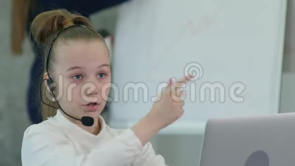 戴着笔记本电脑耳机的漂亮小女孩和她的同事聊天视频的预览图