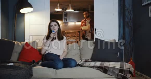 快乐的年轻白种人浪漫夫妇坐在一起在家里度过一个轻松的电影之夜吃零食喝慢动作视频的预览图