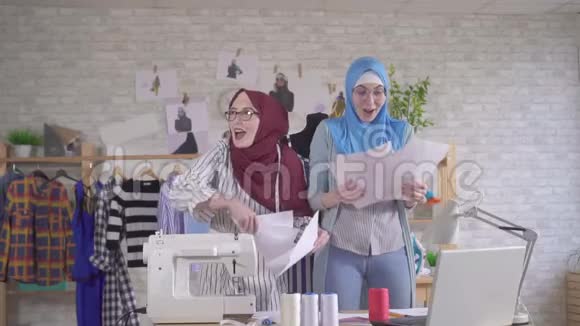 两位积极的穆斯林女青年时装设计师在国家头巾扔文件高兴慢莫视频的预览图